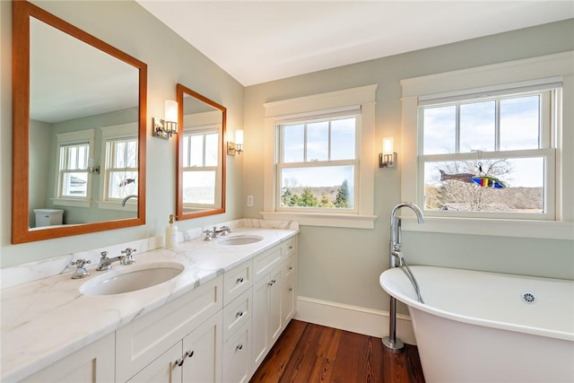 full bath with baseboards, wood finished floors, double vanity, and a sink