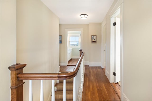 hall with an upstairs landing, baseboards, and dark wood-type flooring