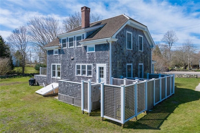 back of house with a chimney, a yard, and roof with shingles