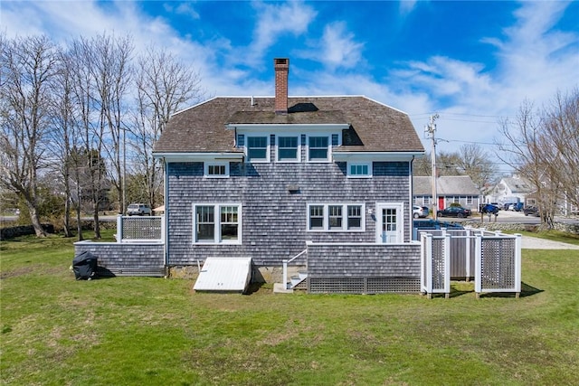 rear view of house with roof with shingles, a yard, and a chimney