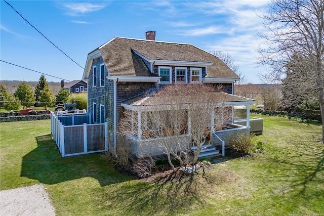 rear view of property featuring a lawn, roof with shingles, a chimney, and covered porch