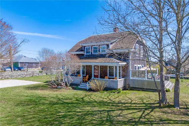 view of front of property featuring a front yard, roof with shingles, covered porch, and a chimney