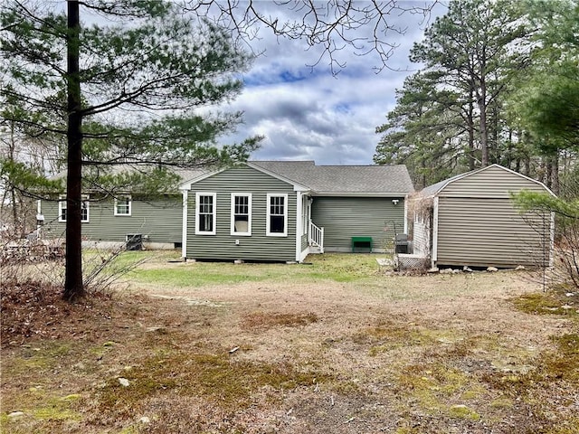 rear view of house featuring a storage unit, an outbuilding, entry steps, a shingled roof, and crawl space