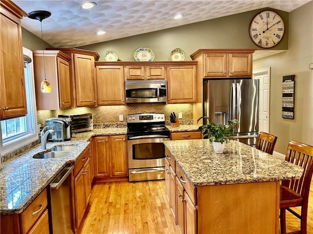 kitchen with a sink, vaulted ceiling, decorative backsplash, brown cabinetry, and appliances with stainless steel finishes