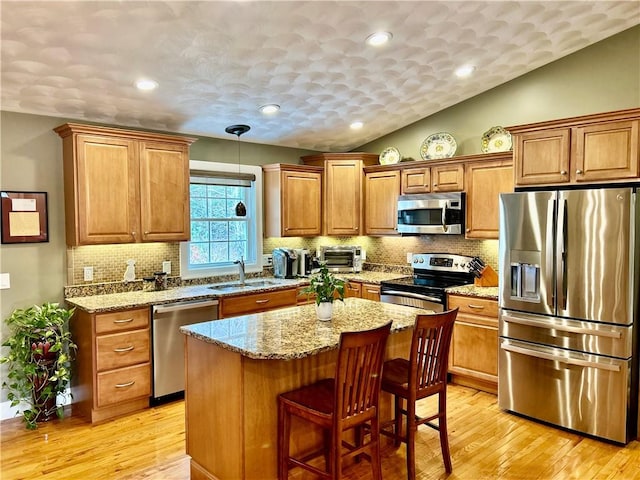 kitchen featuring light stone counters, a sink, brown cabinetry, stainless steel appliances, and light wood finished floors