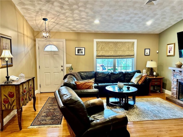 living area featuring a stone fireplace, visible vents, a textured ceiling, and light wood-style floors