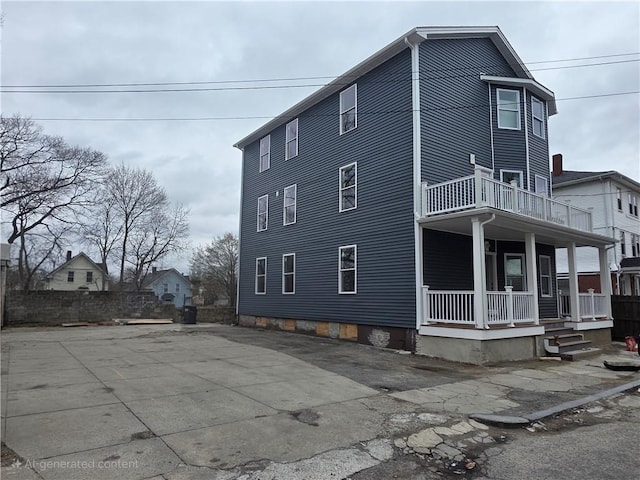 view of side of home featuring fence, a porch, and a balcony