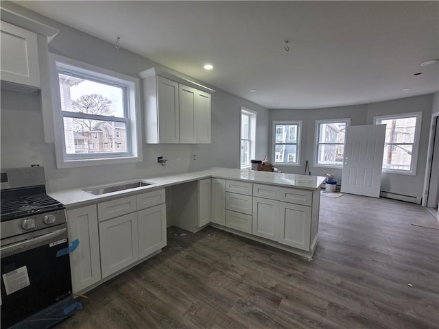 kitchen with dark wood-style flooring, baseboard heating, a sink, stainless steel gas range, and a peninsula