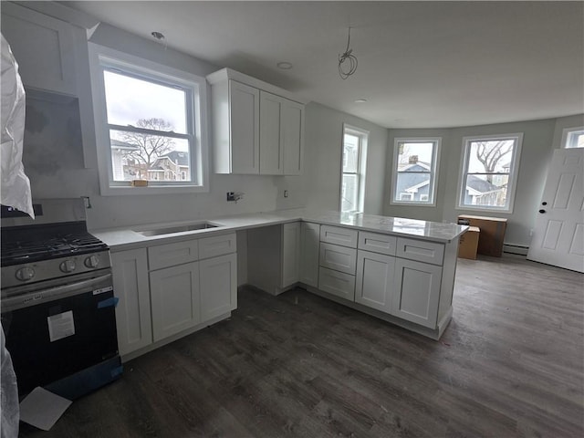 kitchen featuring a baseboard radiator, stainless steel gas range, a peninsula, and dark wood-type flooring
