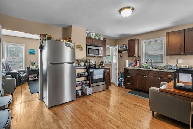 kitchen with light stone counters, stainless steel appliances, a sink, light wood-style floors, and dark brown cabinetry