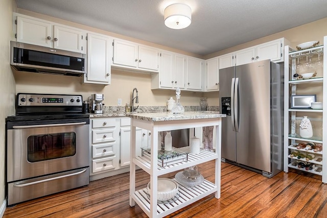 kitchen with appliances with stainless steel finishes, light stone countertops, dark wood-type flooring, and white cabinetry