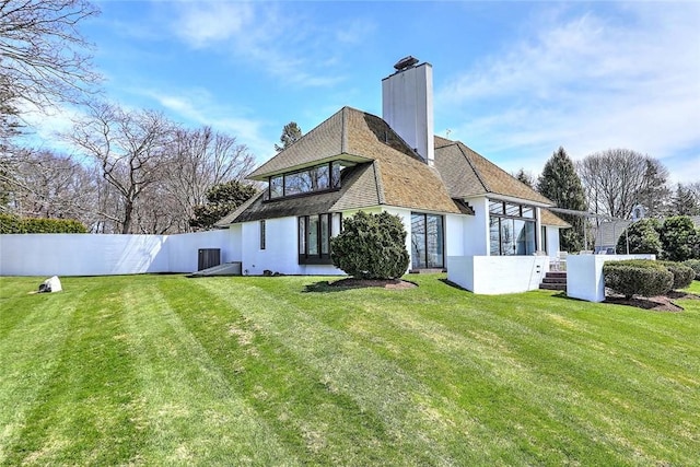 back of house featuring a lawn, a chimney, and fence