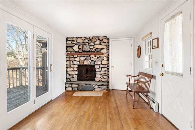 living room with a fireplace, light wood-style floors, a baseboard heating unit, and ornamental molding