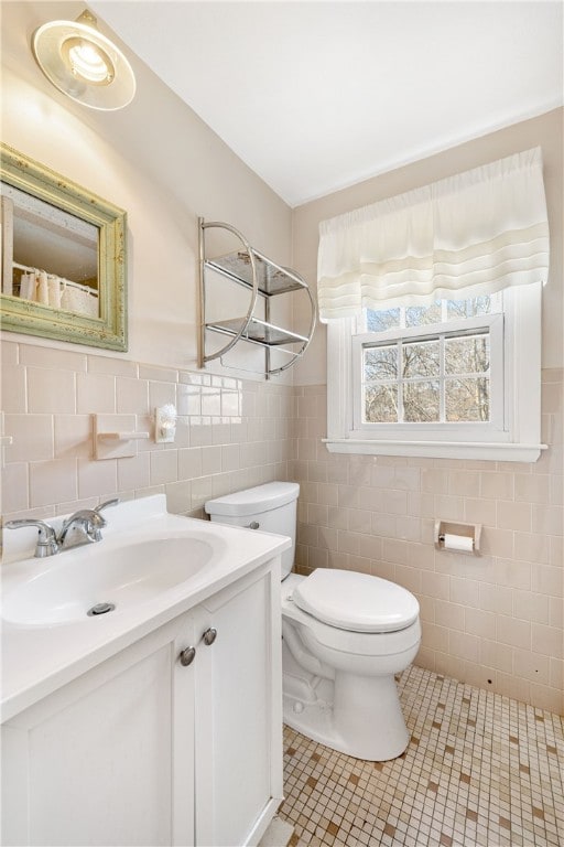 bathroom featuring tile patterned flooring, toilet, vanity, tile walls, and wainscoting