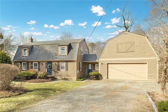 colonial inspired home with a gambrel roof, gravel driveway, a chimney, a shingled roof, and a garage