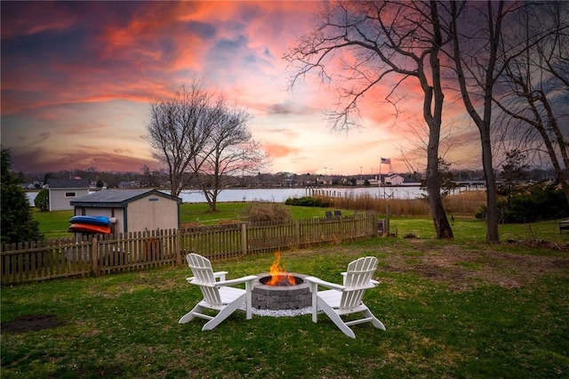 yard at dusk featuring a water view, fence, an outdoor structure, and an outdoor fire pit