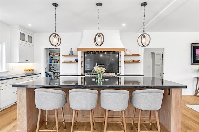 kitchen with an island with sink, open shelves, dark countertops, and refrigerator