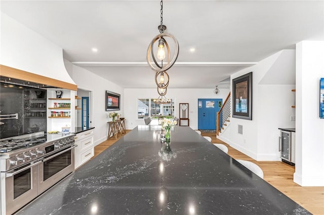 kitchen featuring dark stone counters, light wood-type flooring, double oven range, and beverage cooler