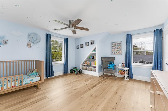 bedroom with light wood-style floors, baseboards, a ceiling fan, and a crib