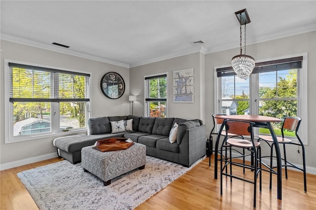 living area with wood finished floors, visible vents, an inviting chandelier, and ornamental molding