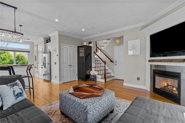 living area with stairway, crown molding, a warm lit fireplace, light wood-type flooring, and recessed lighting
