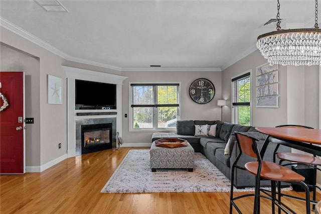 living area with visible vents, baseboards, a chandelier, wood finished floors, and ornamental molding
