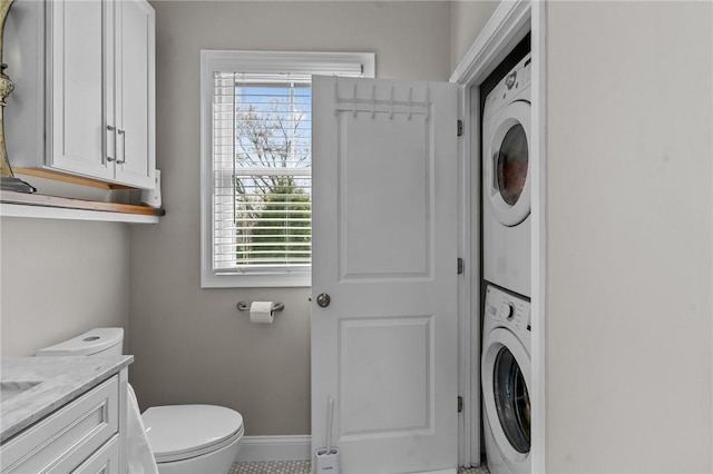 bathroom with stacked washer and dryer, baseboards, vanity, and toilet