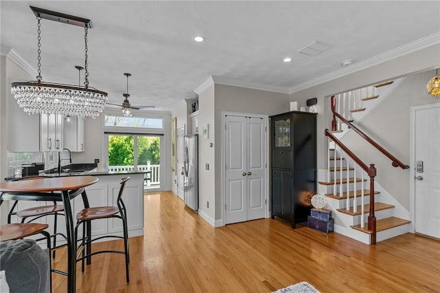 kitchen with a peninsula, light wood-type flooring, freestanding refrigerator, a ceiling fan, and ornamental molding
