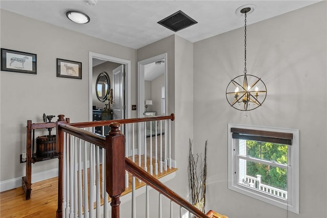 corridor with wood finished floors, an upstairs landing, baseboards, a notable chandelier, and visible vents