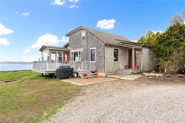 rear view of property with a deck with water view and roof with shingles