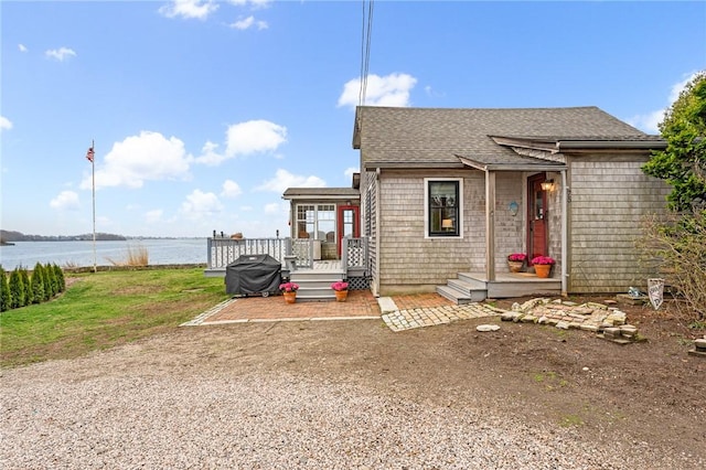view of front of home with a deck with water view and roof with shingles