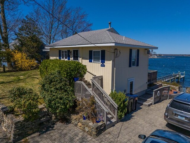 view of front facade with stairway, a patio area, roof with shingles, and a water view