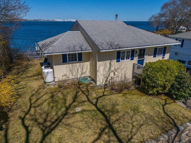 back of house featuring roof with shingles, a water view, and a yard