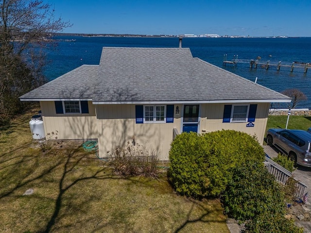 view of front of house with a front lawn, roof with shingles, and a water view