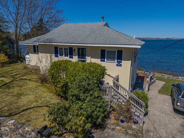 view of front facade with a front yard, roof with shingles, and a water view