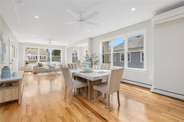 dining space with a ceiling fan, a wall unit AC, a healthy amount of sunlight, and light wood finished floors
