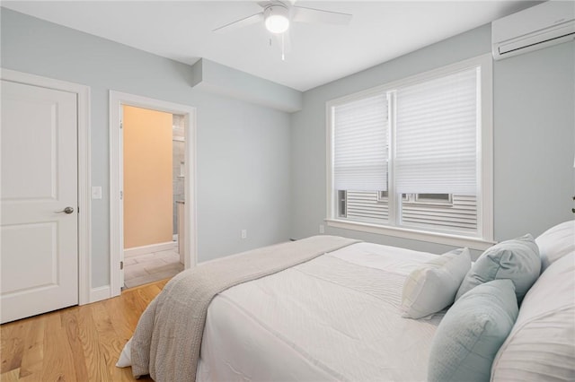 bedroom featuring ceiling fan, a wall mounted AC, light wood-type flooring, and connected bathroom