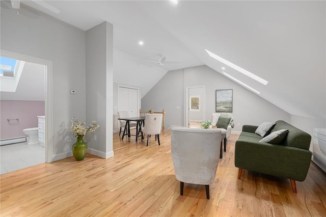 sitting room featuring vaulted ceiling with skylight, light wood-style floors, a ceiling fan, baseboards, and a baseboard radiator