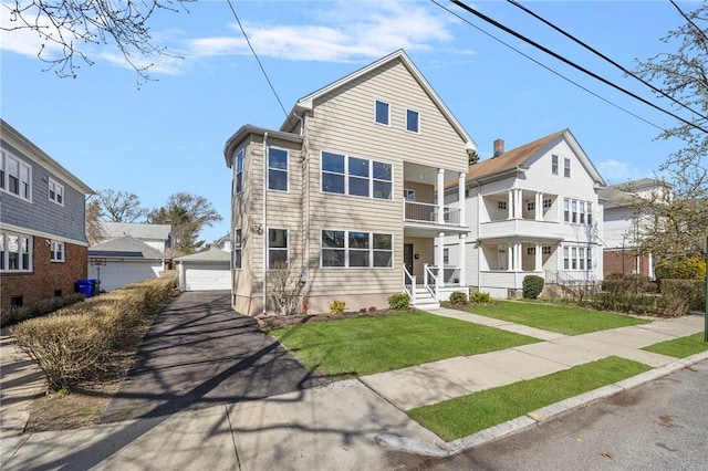 view of front of property featuring a garage, an outdoor structure, a front lawn, and a balcony