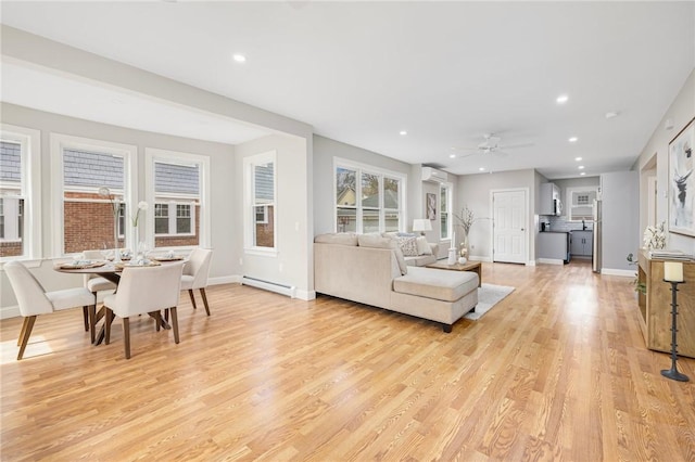living room featuring light wood-type flooring, baseboards, ceiling fan, and a baseboard heating unit
