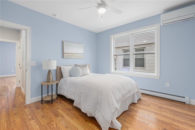bedroom with baseboards, baseboard heating, light wood-style flooring, and a wall unit AC
