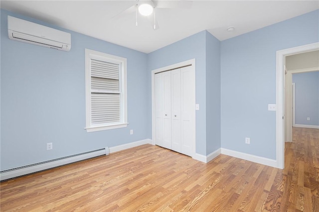 unfurnished bedroom featuring a closet, baseboards, a wall mounted air conditioner, baseboard heating, and light wood-style flooring