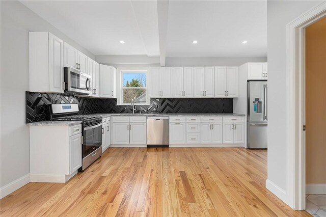 kitchen with white cabinets, appliances with stainless steel finishes, light wood-style flooring, baseboards, and tasteful backsplash