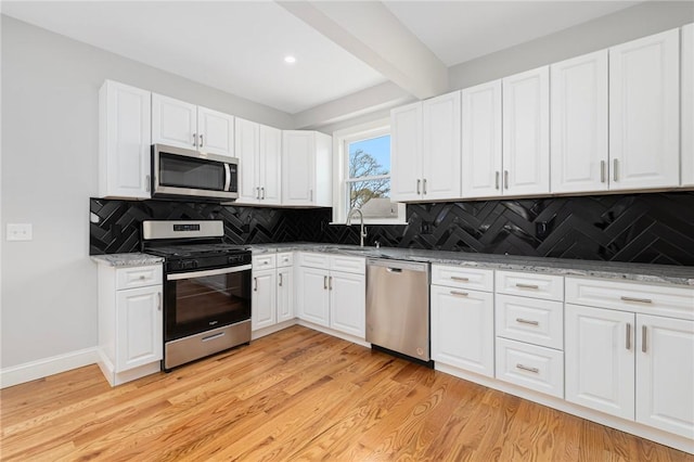 kitchen with backsplash, light wood-type flooring, beam ceiling, a sink, and stainless steel appliances