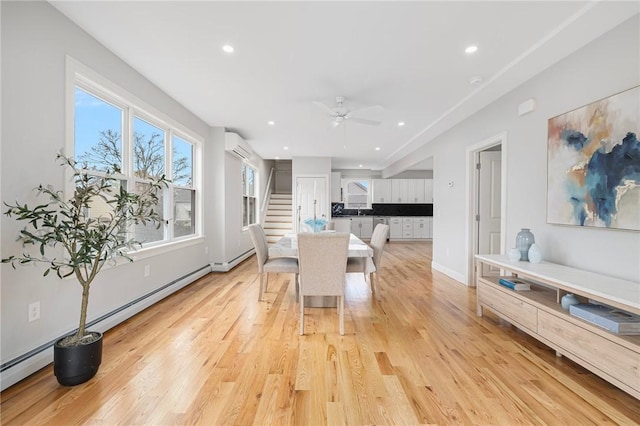 dining area with stairway, a ceiling fan, a baseboard heating unit, and light wood-type flooring