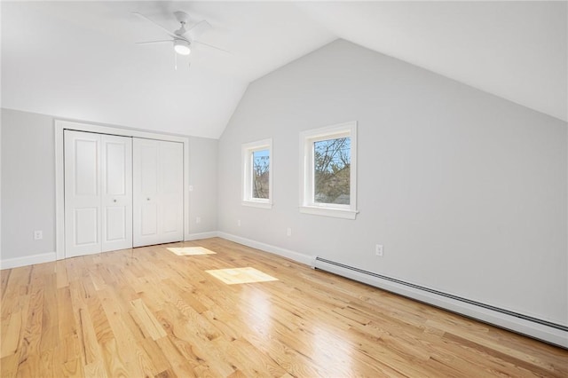 unfurnished bedroom with a closet, vaulted ceiling, wood finished floors, and a baseboard radiator