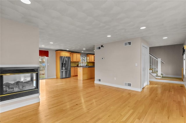 unfurnished living room featuring visible vents, a multi sided fireplace, light wood-type flooring, baseboards, and stairs