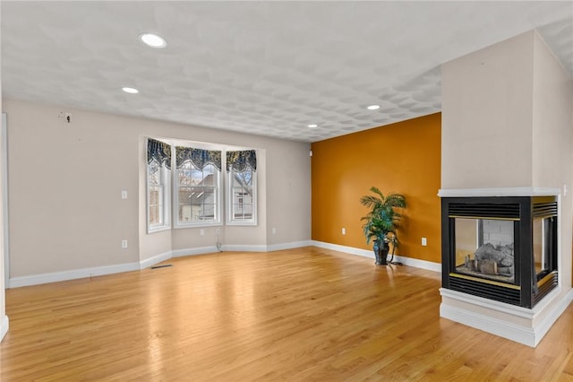 unfurnished living room featuring recessed lighting, light wood-type flooring, baseboards, and a multi sided fireplace