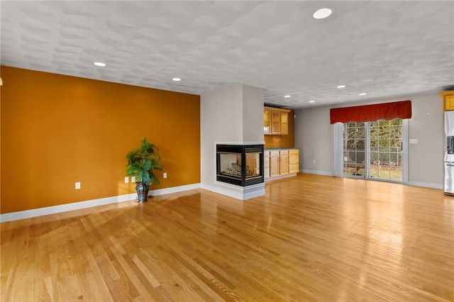 unfurnished living room featuring recessed lighting, baseboards, a multi sided fireplace, and light wood-type flooring