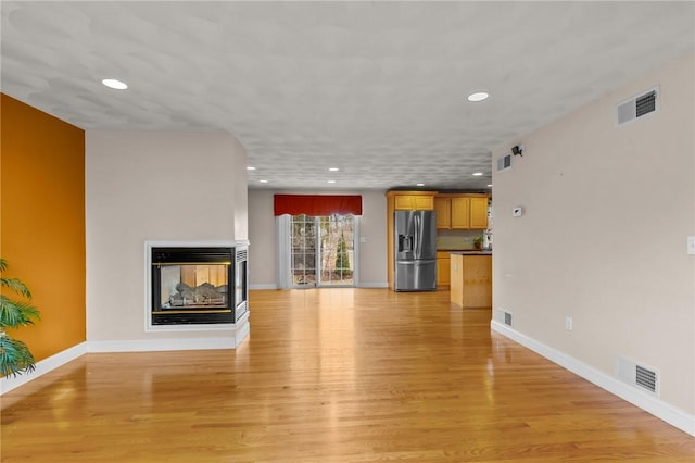 unfurnished living room featuring recessed lighting, a multi sided fireplace, visible vents, and light wood-type flooring